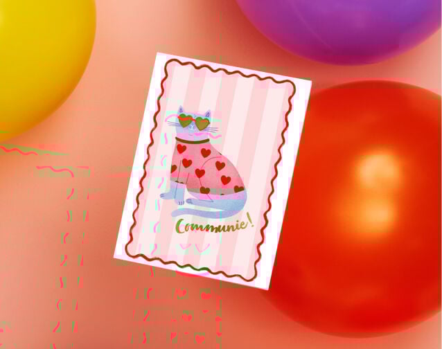 Een communiekaart die ligt tussen gekleurde ballonnen